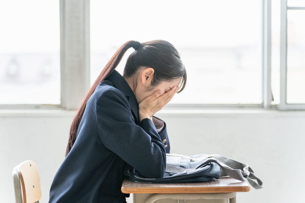 椅子に座って顔を覆っている女子高生