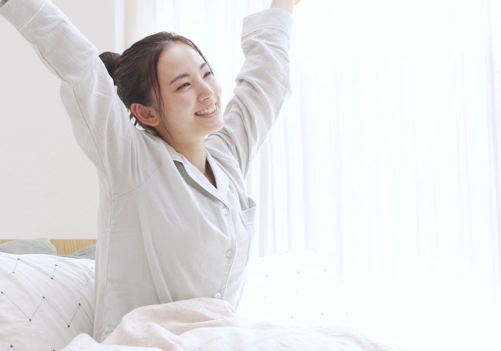 ベッドに座って伸びをしている女性