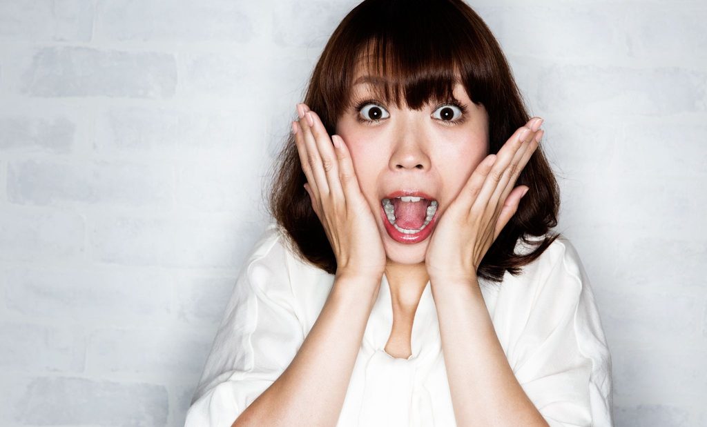 大きく口をあけて両手を頬に当てている女性