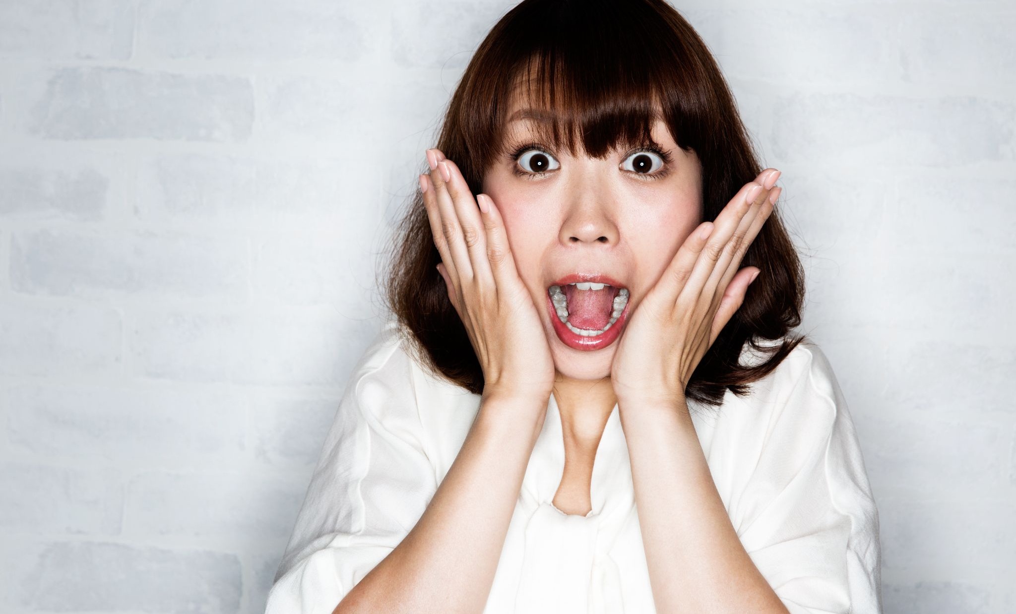 大きく口をあけて両手を頬に当てている女性