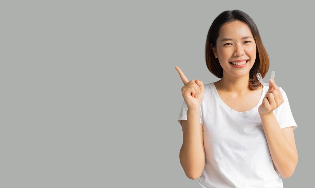 マウスピース矯正装置を持って笑顔の女性が人差し指を立てている