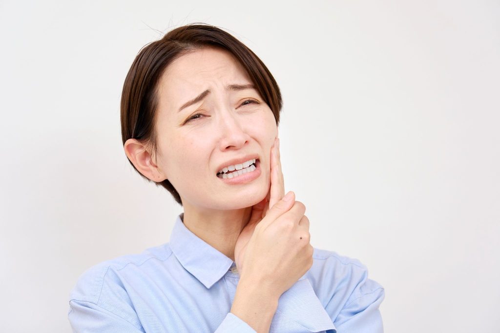 マウスピース矯正中に虫歯ができて頬を押さえている女性